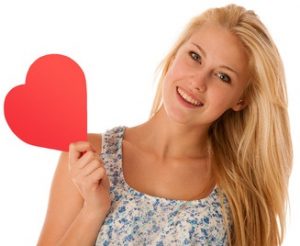 31478611 - beautiful young blonde woman with blue eyes holding red hart banner for valentines day isolated over white